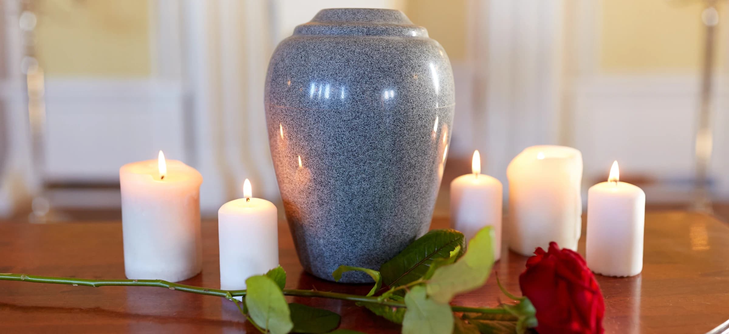 A granite cremation urn on a table with lit candles and a red rose